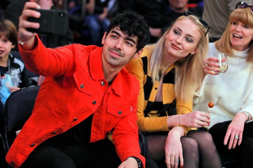 Man wearing a jacket holding out a phone to take a photo with the lady behind him