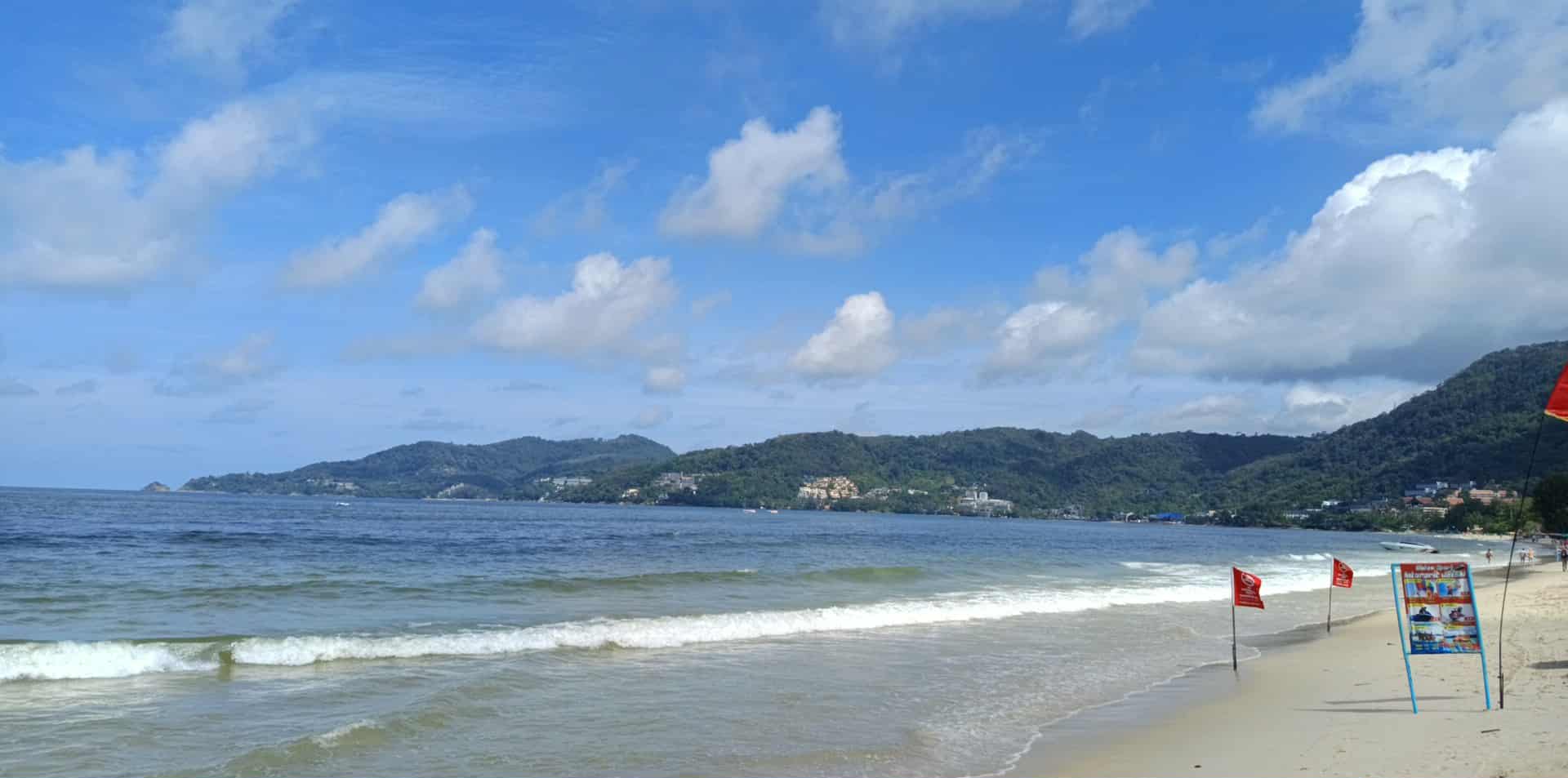 A beach on an island showing swim flags and green canopies and hills.