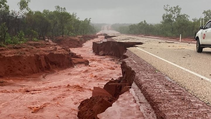 Water rushes through a crumbled section of road 