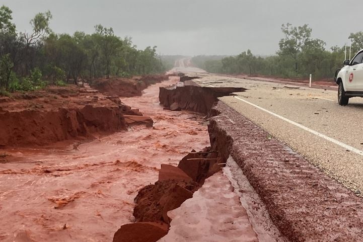Water rushes through a crumbled section of road 