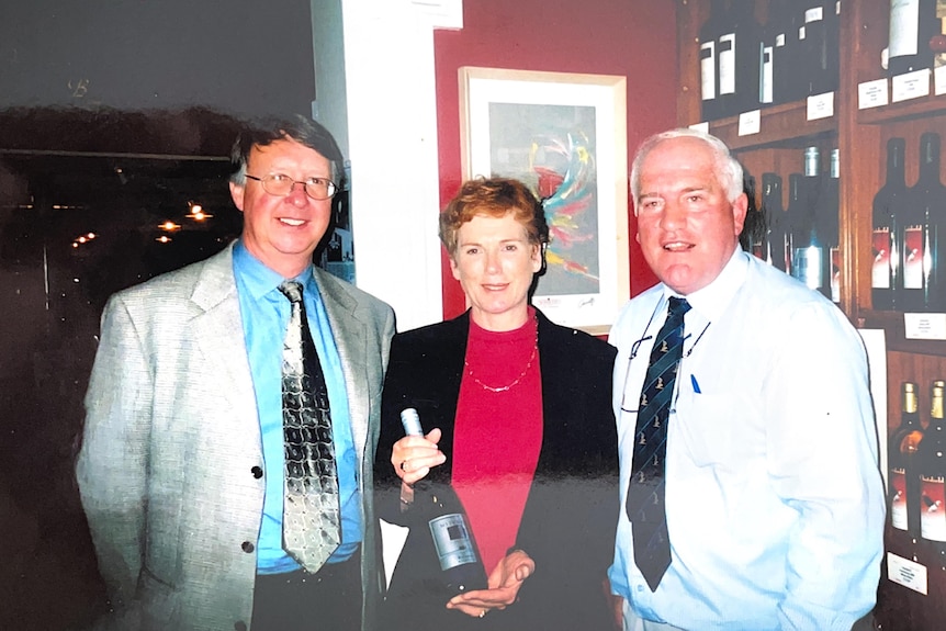 Andrew and Jane Mitchell hold a bottle of their wine in a bottle shop in Ireland with the store owner, Johnathon. 