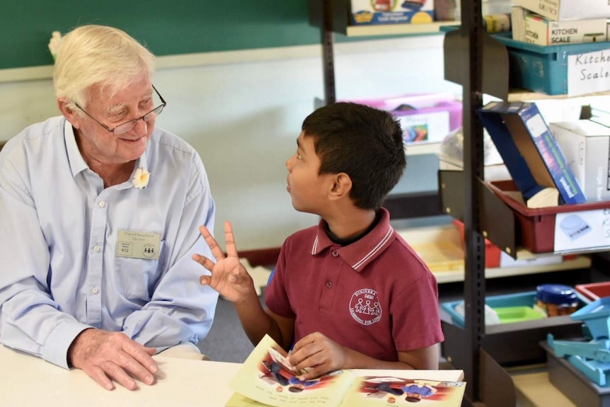 An older man helps a child with his reading.