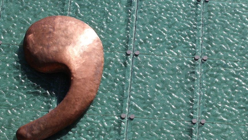 A bronze apostrophe sign on the roof of a building.