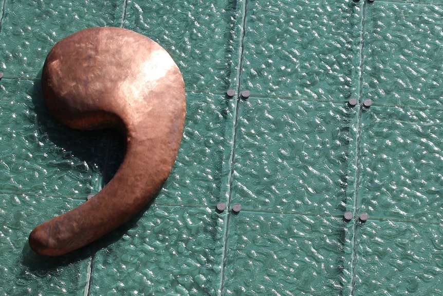 A bronze apostrophe sign on the roof of a building.