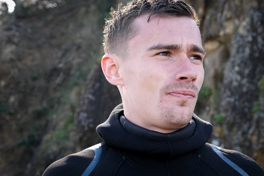 Close up from low angle of young man in wetsuit looking into distance