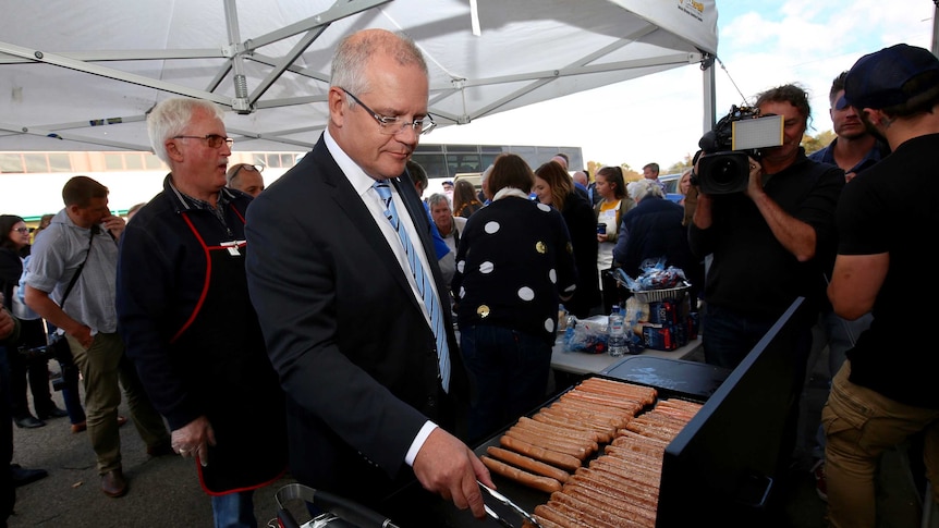 Scott Morrison cooks sausages on a barbecue surrounded by media