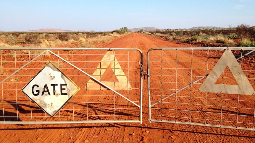 A metal gate blocks a long red dust road