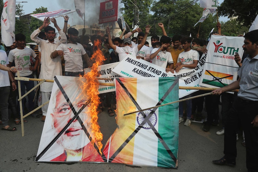 Pakistanis burn a poster of Indian Prime Minster Narendra Modi while holding signs about Kashmir.