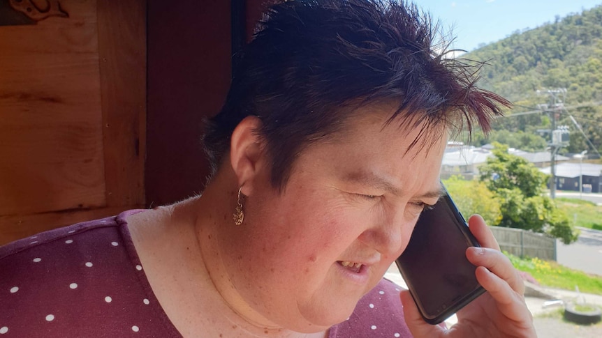 Woman with short red hair, wearing a red shirt with white polka dots talking on a mobile phone outside of a house