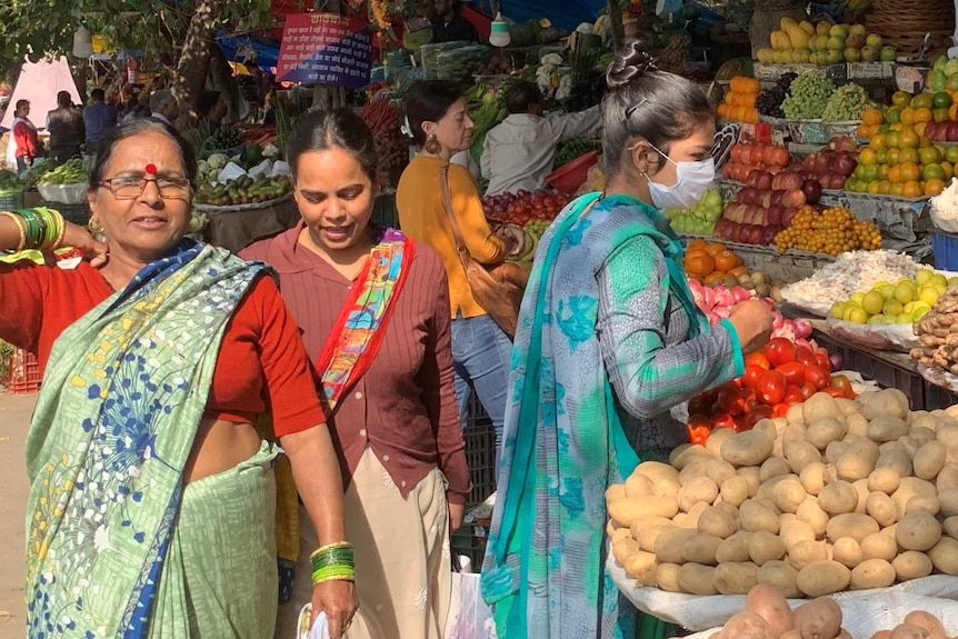 Women walk through an Indian food market while a man hold limes