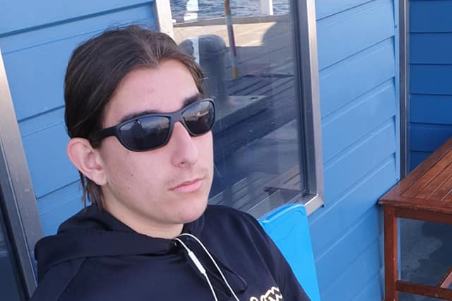 A teenager in sunglasses sitting on a blue chair.