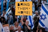 A man stands in a crowd of Israeli supporters holding a yellow and black signs with the words 'Bring them Home' on it