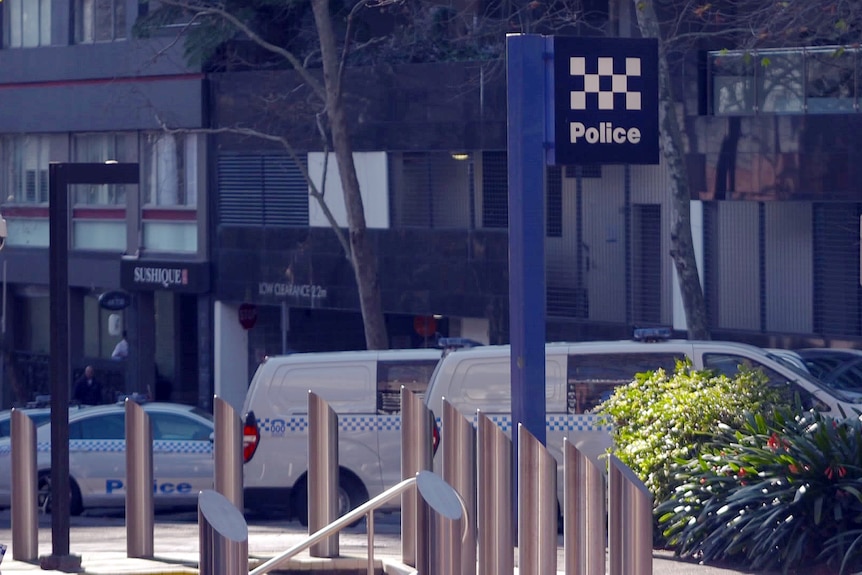 the outside of a sydney police station with cars and police vans parked along the street