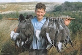 An early-teens boy smiling with a stick of harvested mutton birds across his shoulders