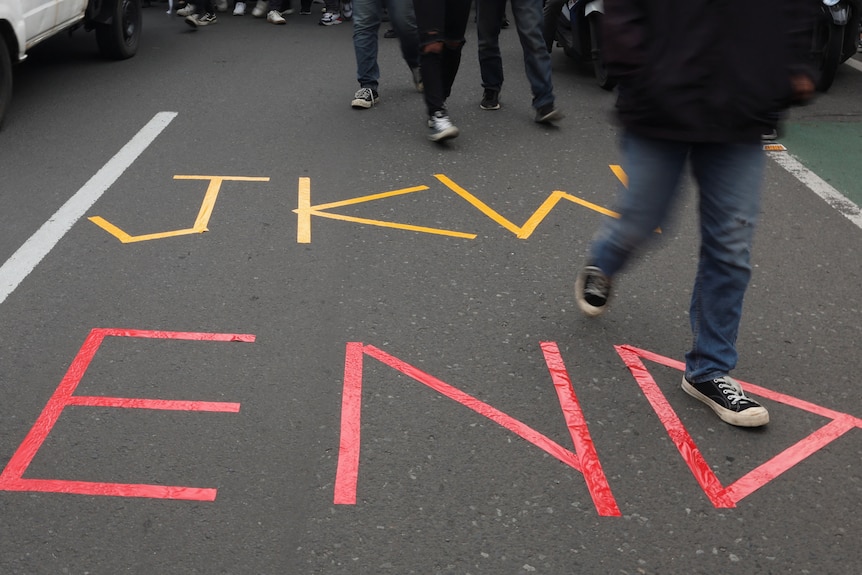 Des étudiants universitaires passent devant un panneau « JKW END » collé sur la route.