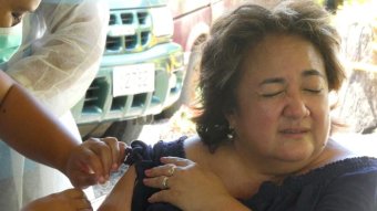 A woman grimaces as she is injected in the arm