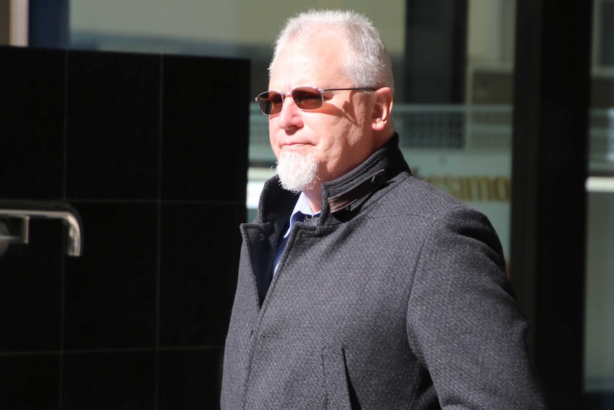 A midshot of contractor Philip Stephen Wood walking outside wearing a grey coat and sunglasses.