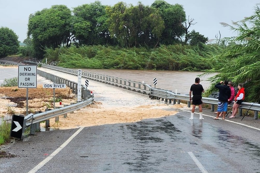 Four people standing on a road near a bridge over the Don River that's covered by floodwaters.