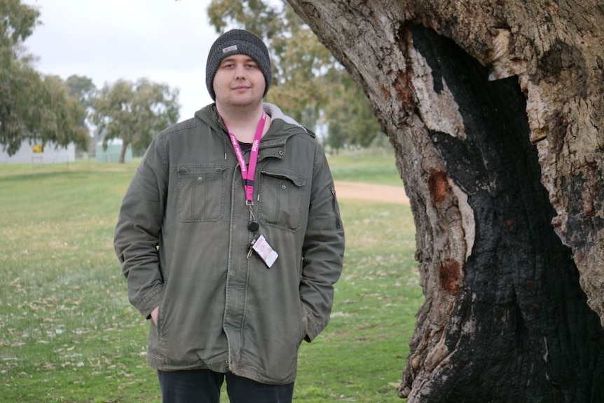 A man in a coat and a beanie standing by a tree