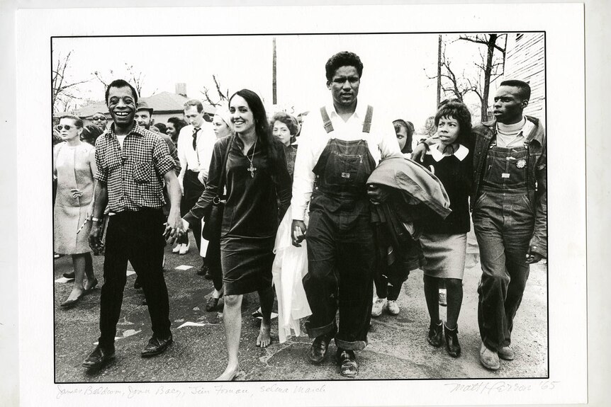 A black and white photo of Joan Baez marching with civil rights protesters in 1965