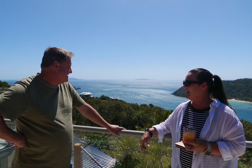 Couple stand on veranda overlooking view of Keswick Island. 