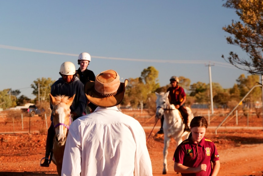 A man in a hat leads three young girls who are riding horses. 