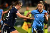 A Sydney FC W-League player dribbles the ball as a Melbourne Victory opponent runs alongside her.
