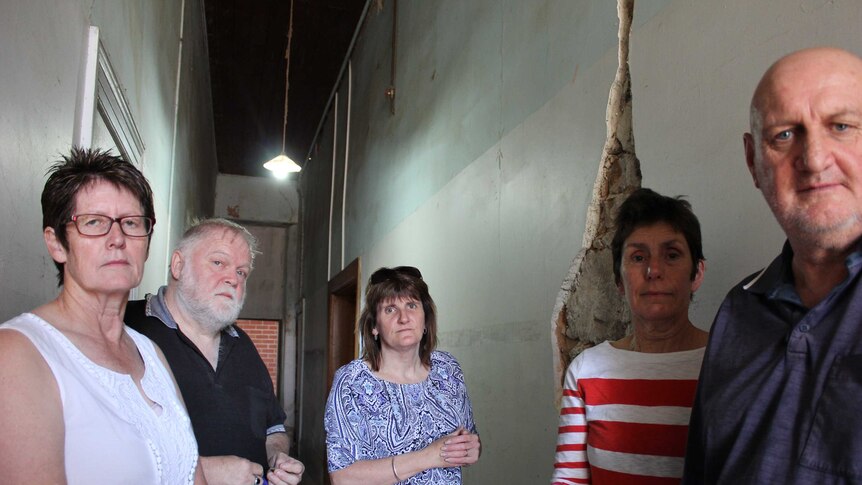 A group of people stand in front of a damaged wall.
