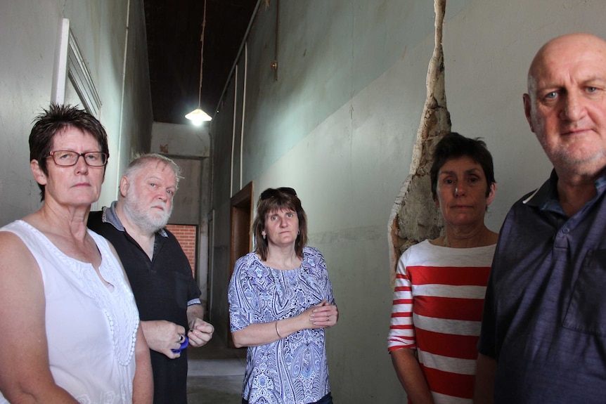 A group of people stand in front of a damaged wall.