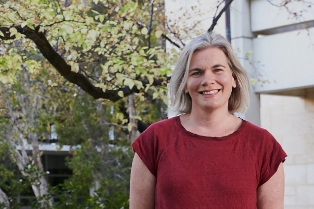 A woman smiles in front of a tree