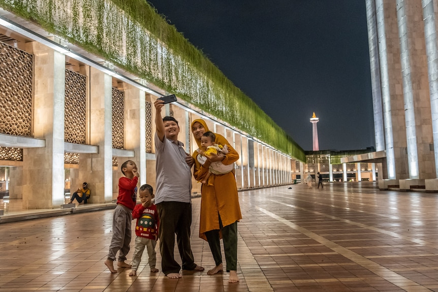 An Indonesian family takes a selfie inside a mosque with a flame sculpture in the background