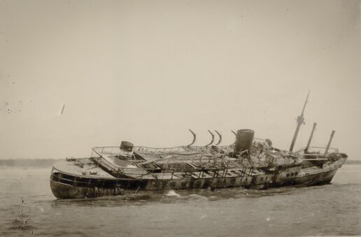 Burned ship in shallow water listing to starboard.
