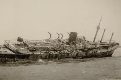 Burned ship in shallow water listing to starboard.