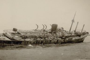 Burned ship in shallow water listing to starboard.