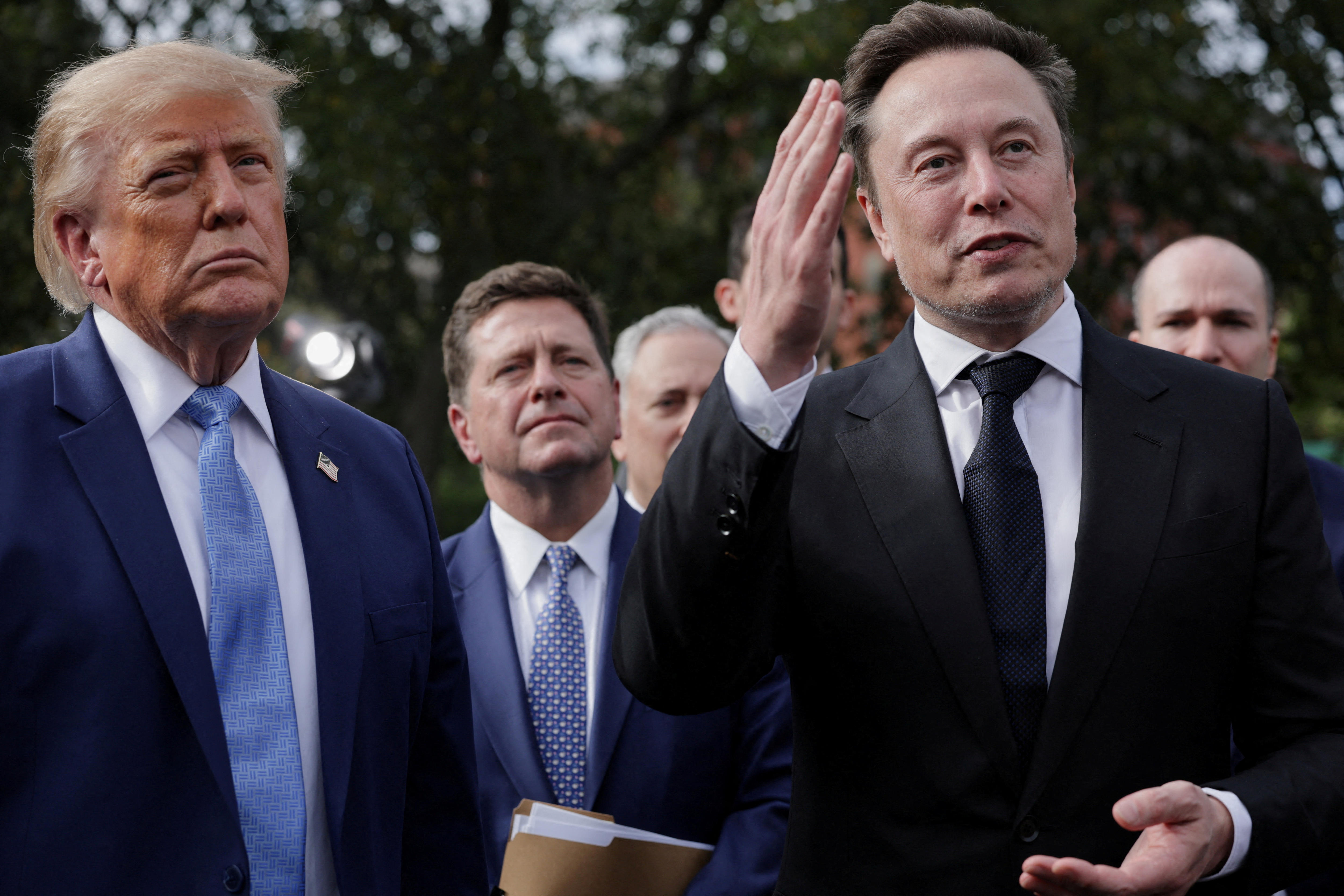 Musk gestures with one hand as he and Trump speak to reporters outside.