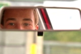 Young driver looks in rear view mirror of car