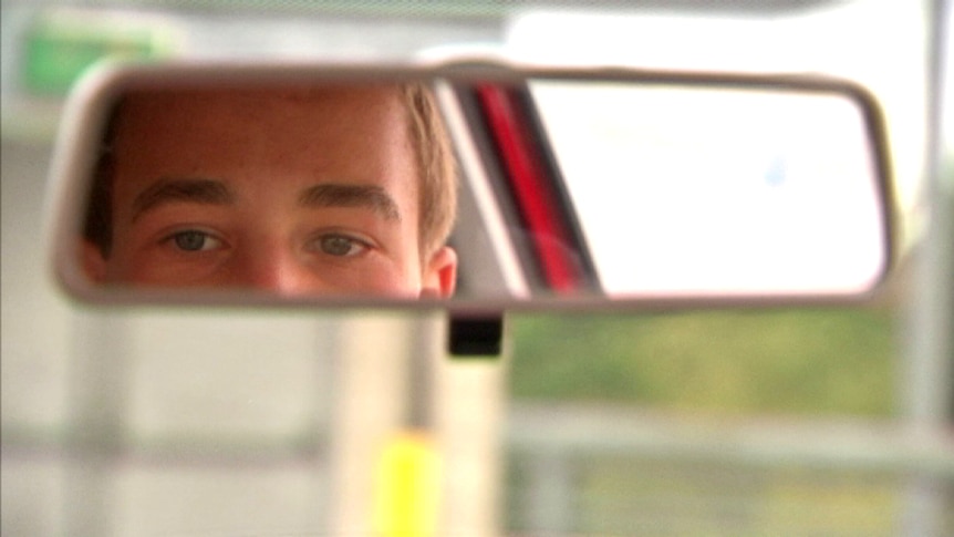 Young driver looks in rear view mirror of car
