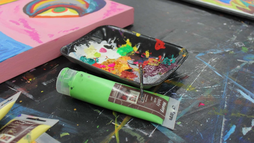 A tube of paint next to a black tray with different splodges of paint.