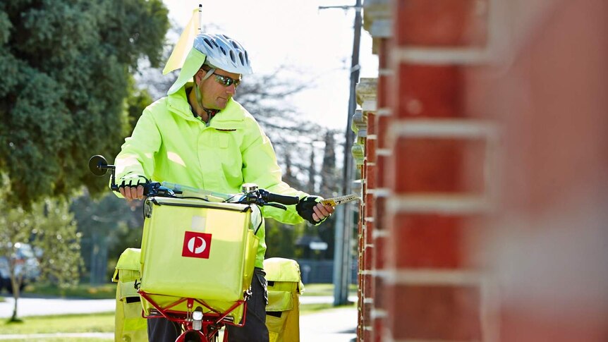 An Australia Post worker delivers mail into a letterbox riding an electric bicycle.