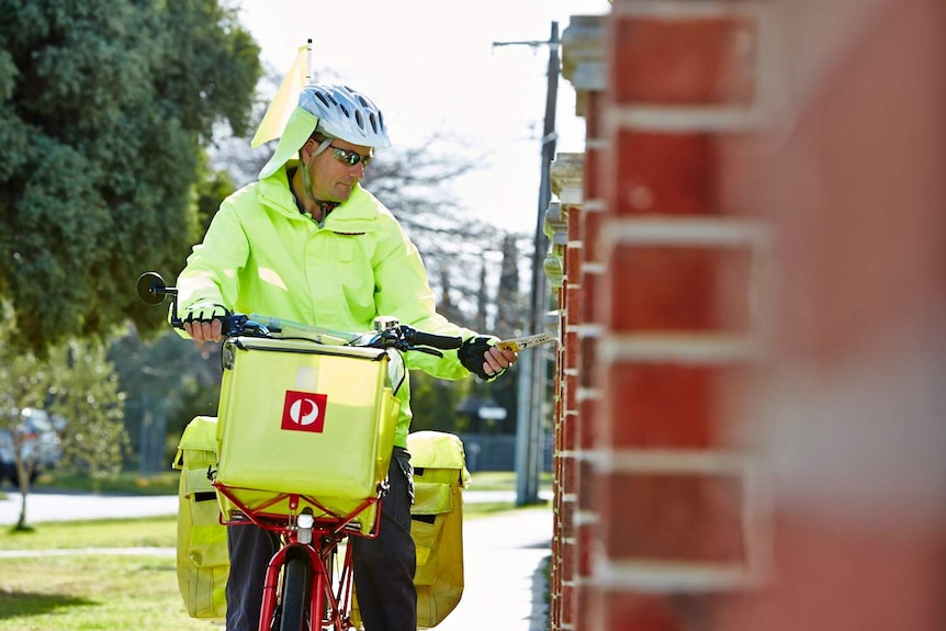 An Australia Post worker delivers mail into a letterbox riding an electric bicycle.