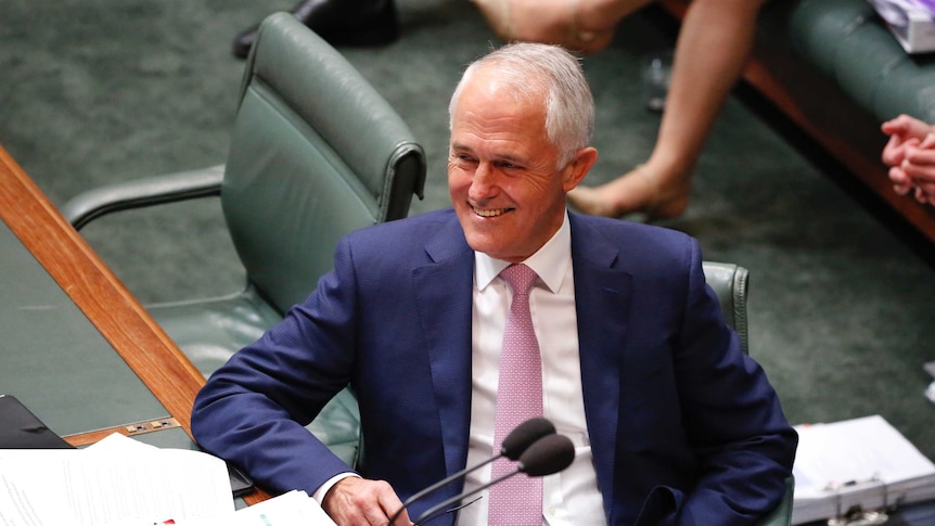 Prime Minister Malcolm Turnbull smiles and holds his glasses in his right hand during Question Time