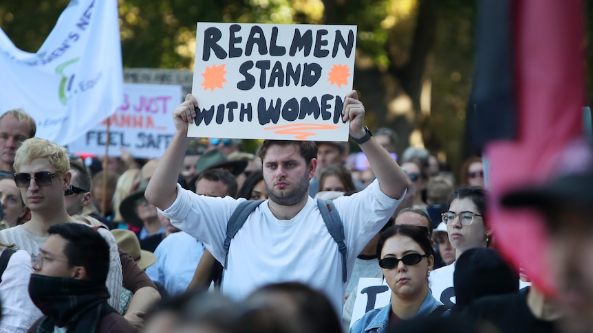 Man holds sign saying 'real men stand with women' at the violence against women rally in Sydney.