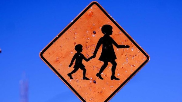 An orange school zone sign against a blue sky