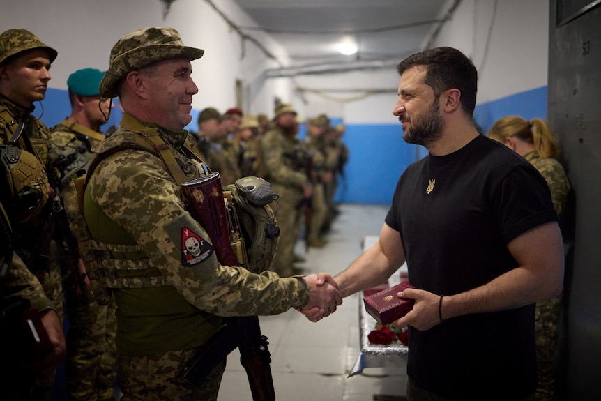 Man in black shakes hand with man in army camouflage 