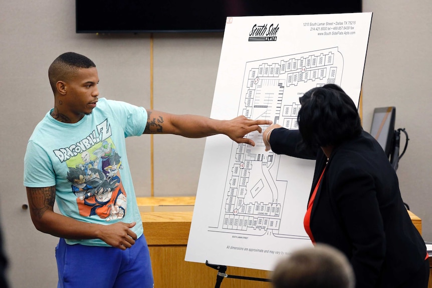 A man in a light blue t-shirt points to a map of an apartment building.