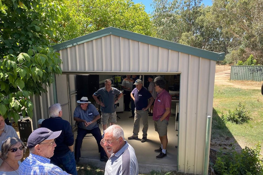 A Colorbond shed with plenty of older men standing around in it.