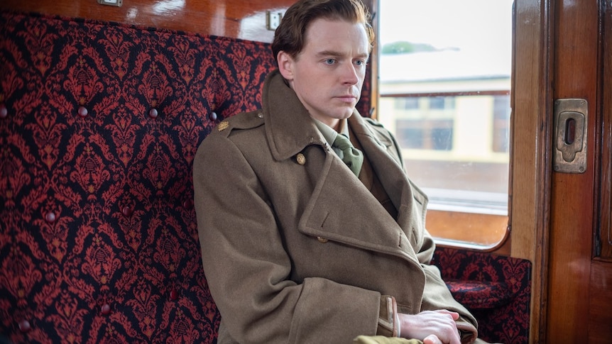 man in army greatcoat on a train with red seats