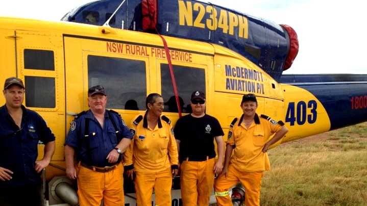 A group of people wearing yellow uniforms stand in front of a helicopter.