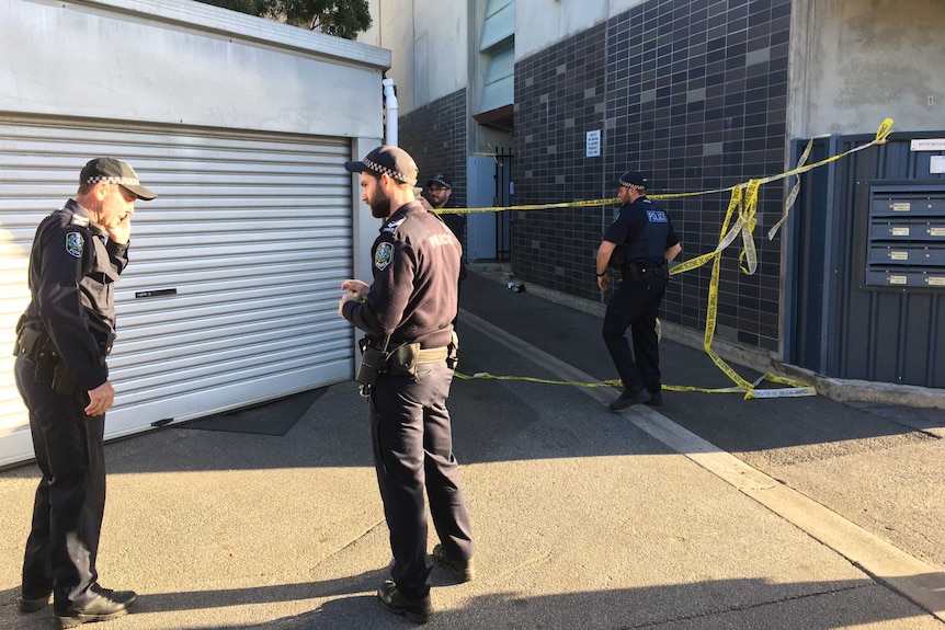 Police officers stand in front of a building with yellow crime tape behind them