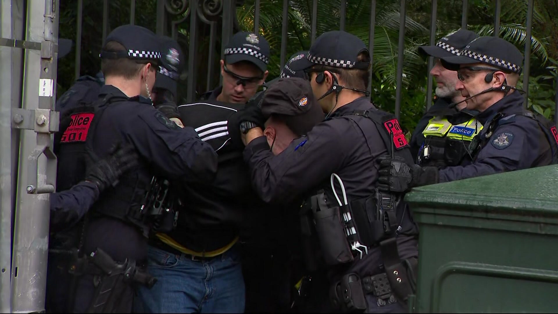 A person dressed in dark clothes being detained by several police officers.